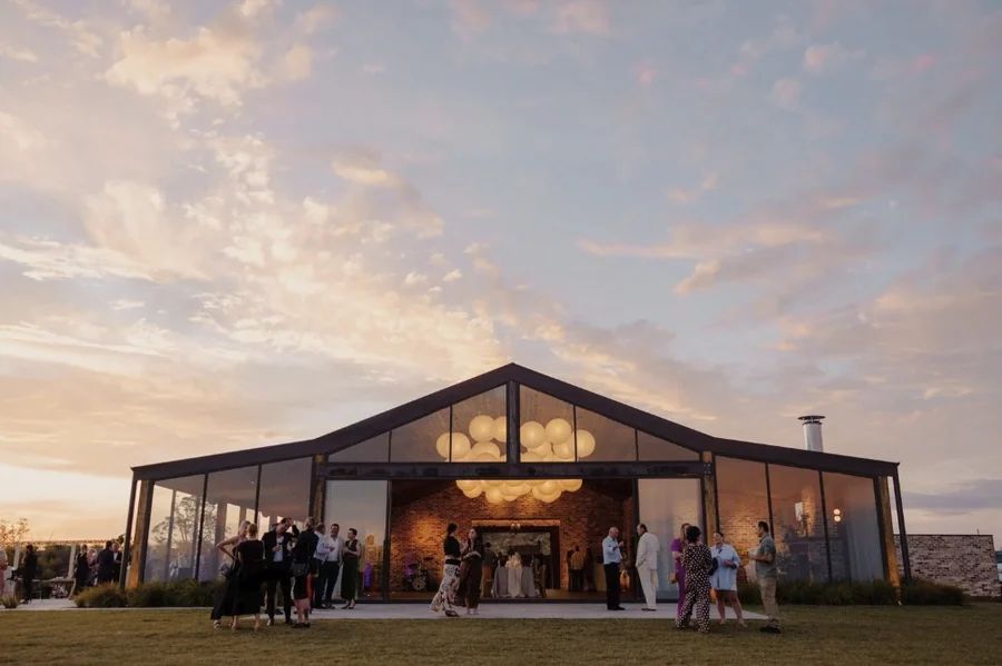 The glass barn at Caoura Cliffs lit at dusk with guests arriving