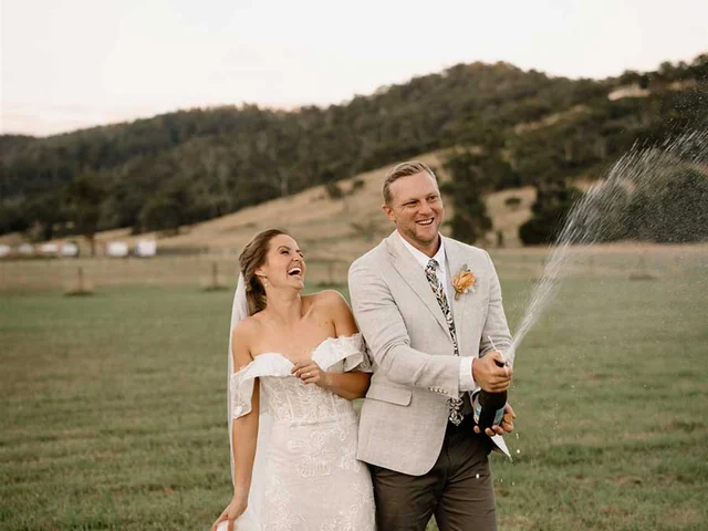 Groom sprays champagne beside the bride on the estate lawn
