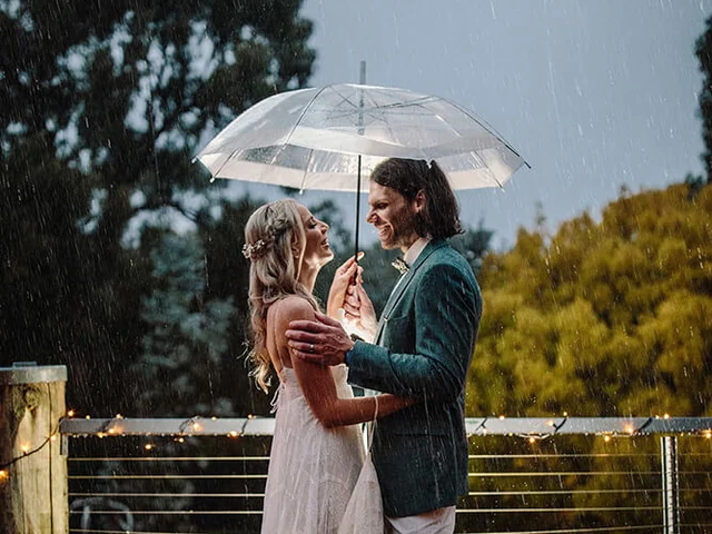 Couple under a clear umbrella on the deck on a rainy wedding day