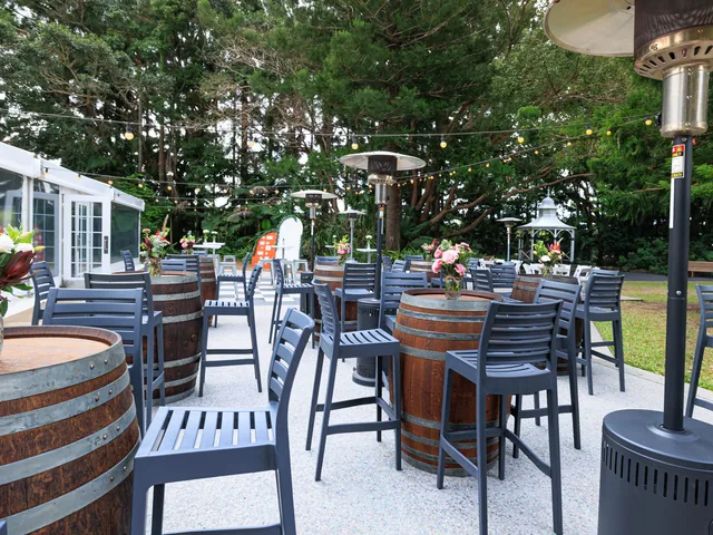 In The Grove — covered patio seating with barrel tables beside the marquee