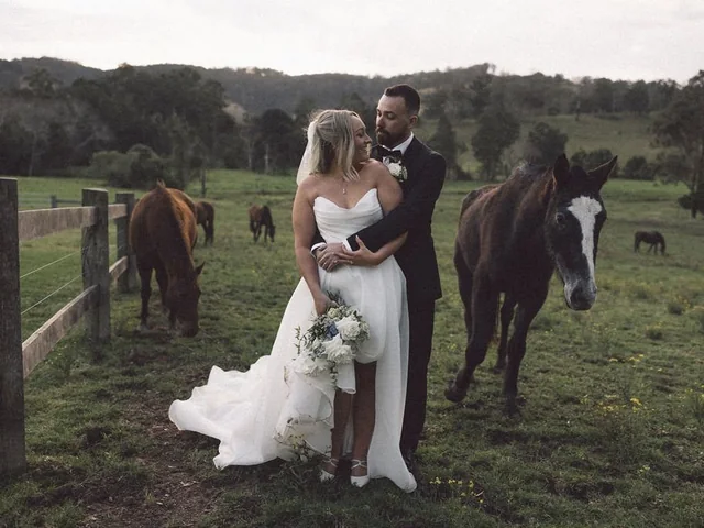A bride and groom by the fence with the farm horses at Wallaringa Farm