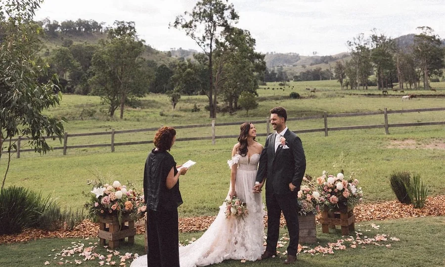 An elopement ceremony with a celebrant on the lawn, with the paddocks and hills of Wallaringa Farm behind
