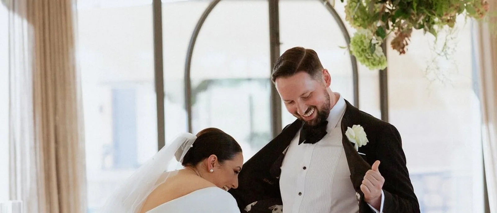 Groom in a white dinner jacket laughing with his bride