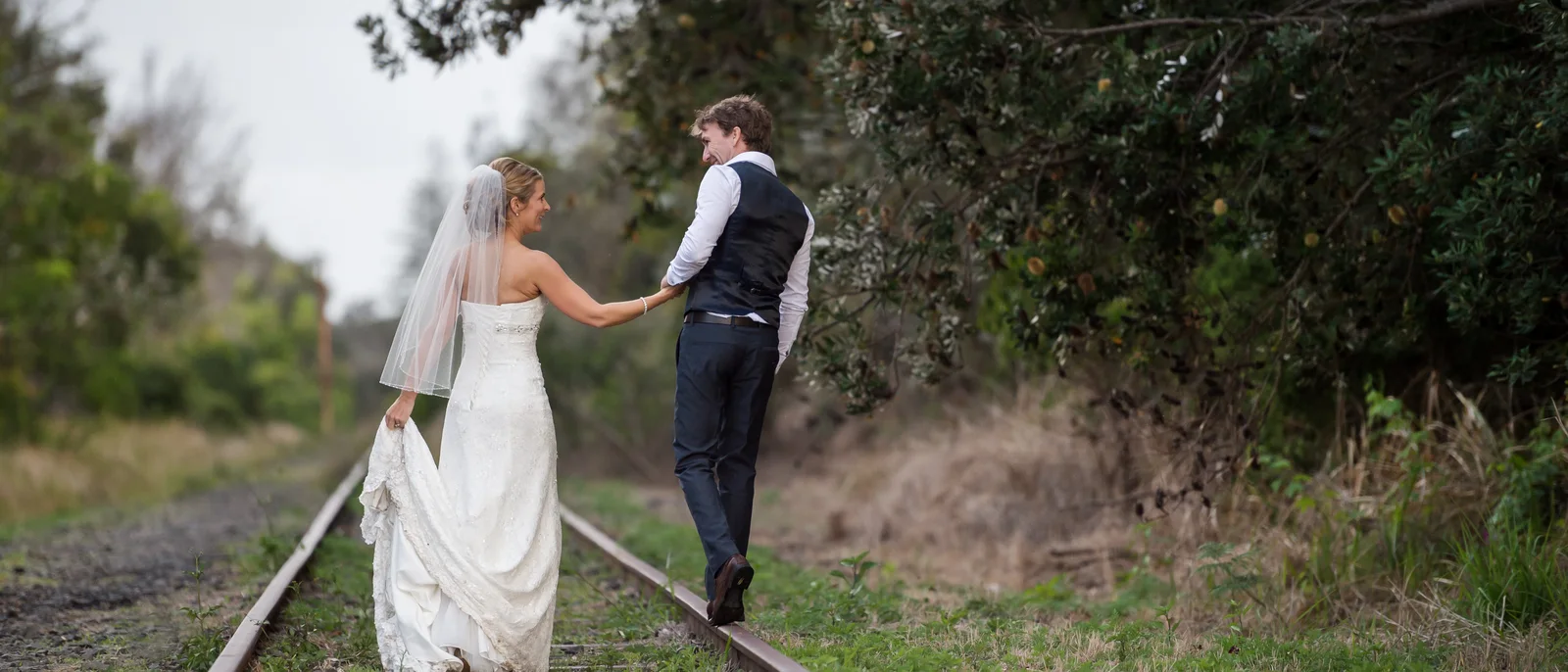 Bride and groom walking along a railway line
