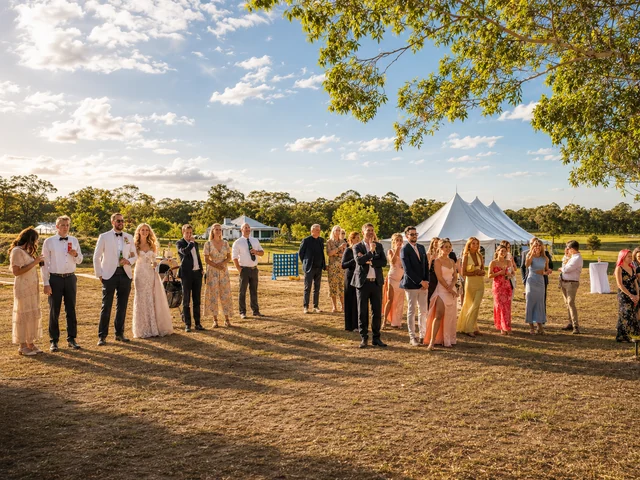 Wedding guests gathered on the lawn with marquee and farmhouse views behind them