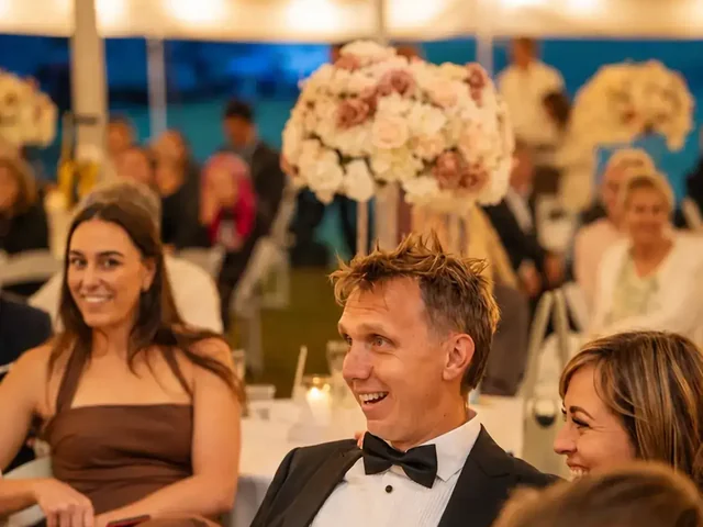 Wedding guests seated under festoon lights and tall floral centrepieces during a marquee reception at Adeline Estate