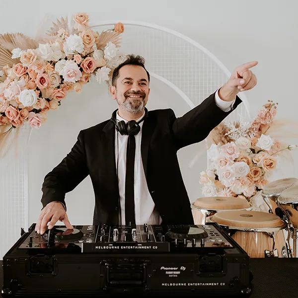 Melbourne Entertainment Company: DJ pointing to the crowd beside a floral arch