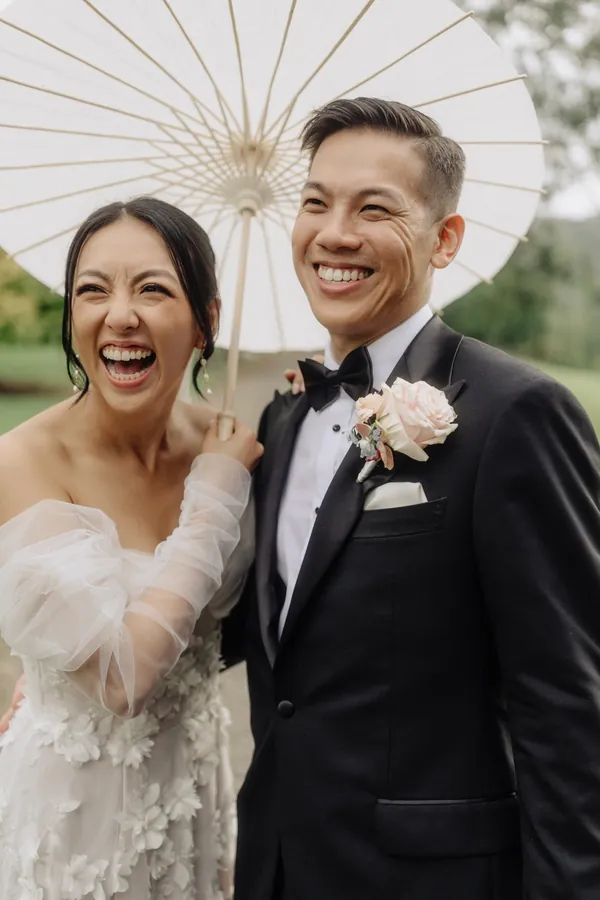 Fable Weddings: Laughing bride and groom under a paper parasol