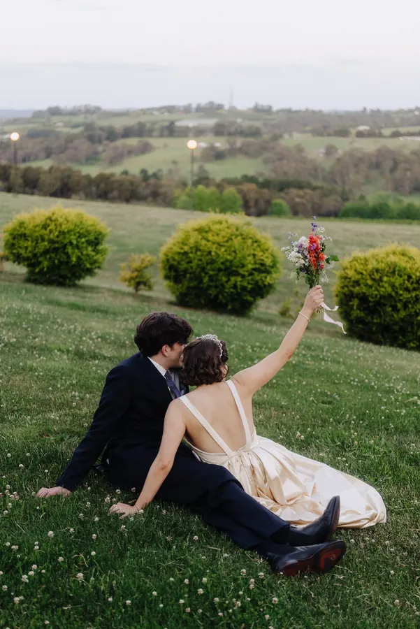 Fable Weddings: Couple relaxing on a grassy hillside with a bouquet