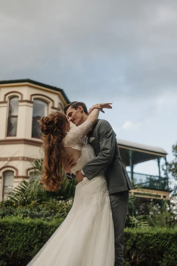 Fable Weddings: Bride and groom kissing in front of a heritage homestead