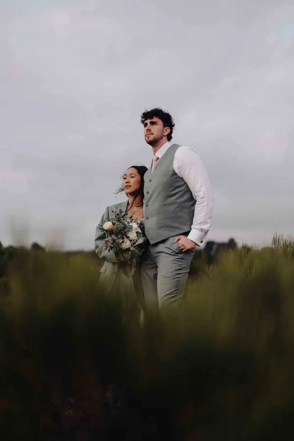 Fable Weddings: Couple standing together in tall grass under a moody sky