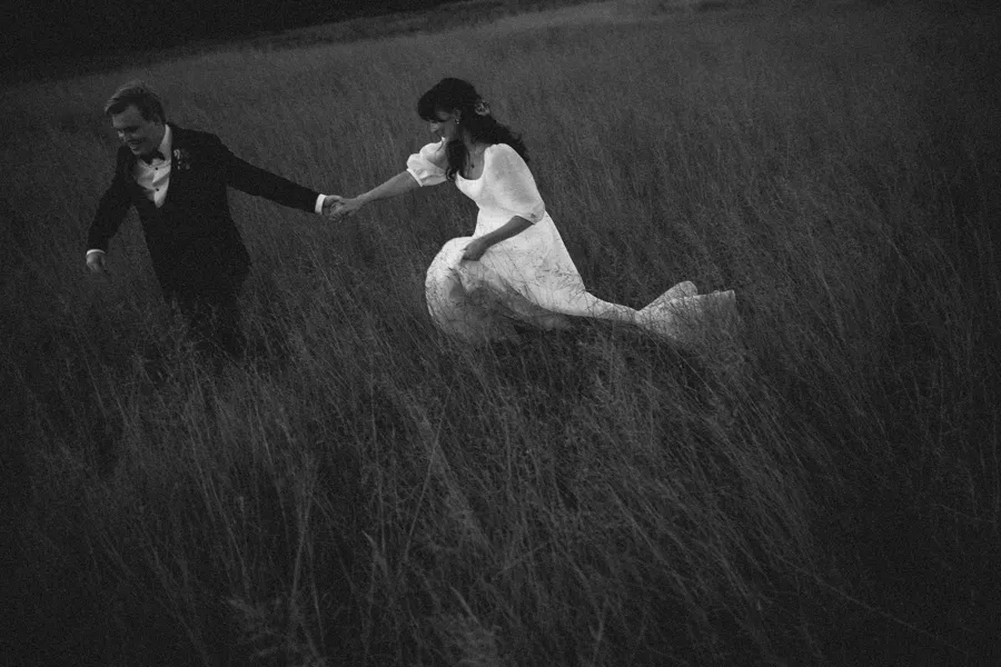 Rogue Weddings: the couple running through long grass in black and white