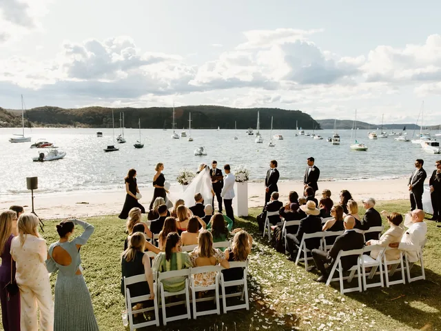 Lovesick Weddings: Harbourside ceremony set up on a beach lawn with white chairs and an arch