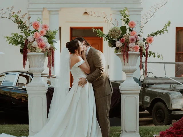 Lovesick Weddings: Couple kiss in front of a heritage house with floral plinths