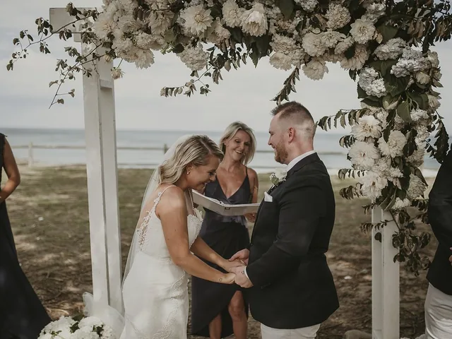 Lovesick Weddings: Couple exchange vows under a white floral arch by the water